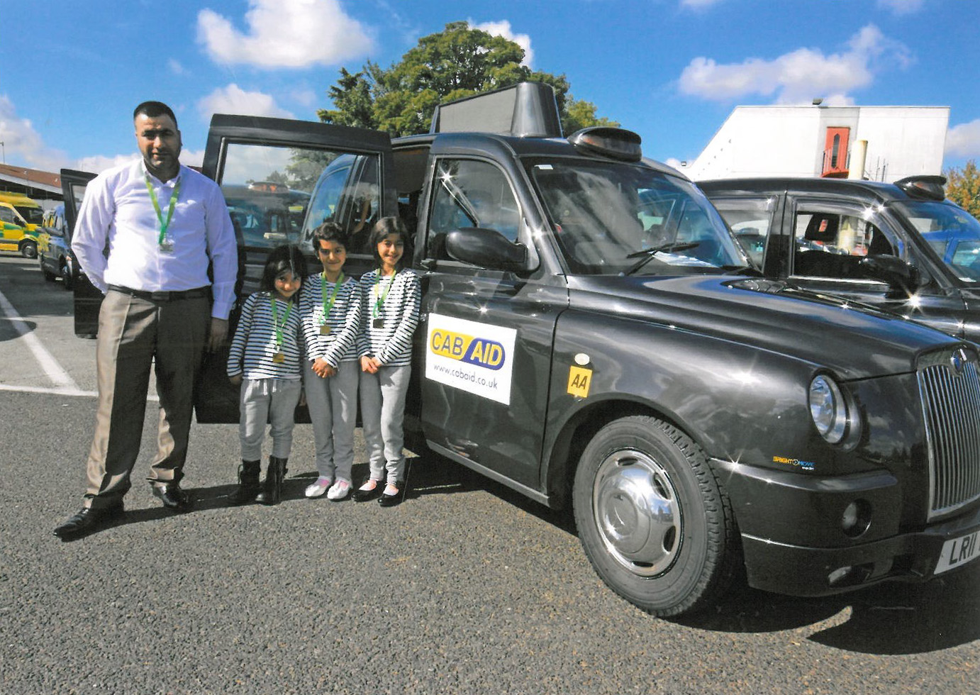 Three children in matching outfits excitedly entering the open door of a black taxi.